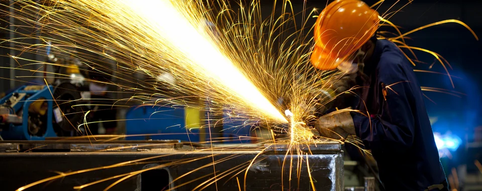 Worker grinding metal with sparks flying in a high heat industrial work environment